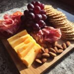 A simple 5 minute charcuterie board featuring sliced cheese, salami, prosciutto, grapes, almonds, and crackers.