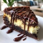 A rich slice of brownie cheesecake, layered with creamy cheesecake and topped with a decadent chocolate drizzle.