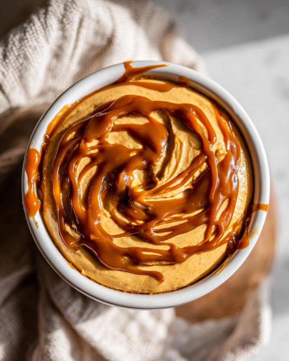 Close-up of an Irresistible Easy Caramel Pumpkin Pie Cheesecake Dip in a white bowl, drizzled with caramel sauce.