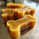 Close-up of golden chamomile honey gelatin bones, shaped like dog biscuits, on a metallic surface.