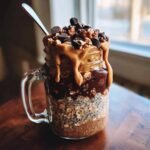 A delicious jar of Chocolate Peanut Butter Overnight Oats topped with chocolate chips, nuts, and peanut butter drizzle.