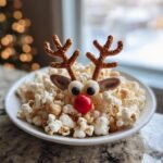 A fun holiday treat shaped like a reindeer's face using popcorn, pretzels, candy eyes, and a red nose.