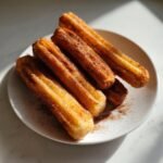A plate of freshly made Crispy Air Fryer Churros coated in cinnamon sugar, ready to be enjoyed.