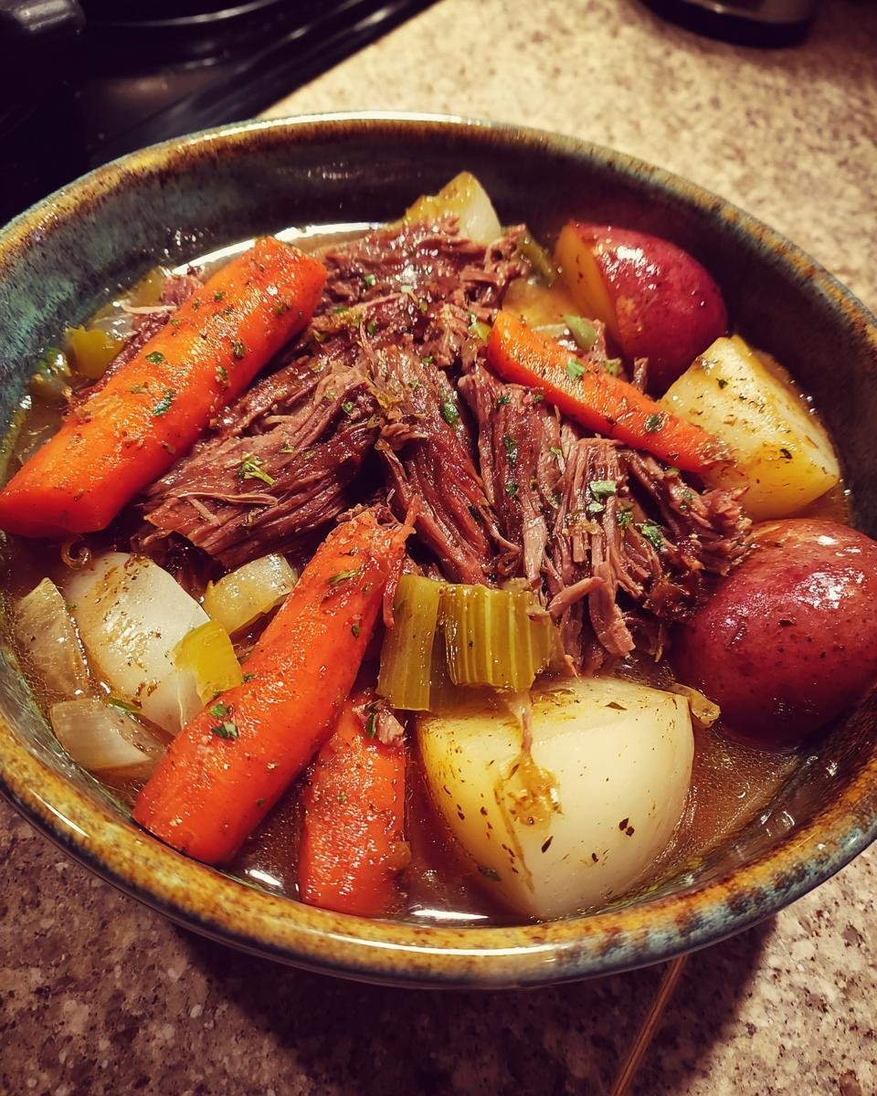 A close-up bowl of tender crock pot pot roast with carrots, potatoes, and celery in rich gravy.