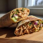 Close-up of two halves of a delicious turkey wrap, showcasing shredded turkey, fresh vegetables, and herbs.
