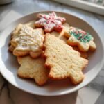 A plate filled with assorted shapes of diabetic friendly Christmas cookies, including trees and snowflakes, some decorated.