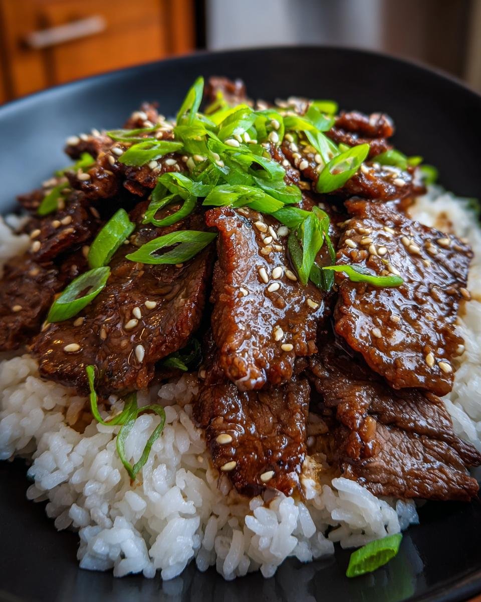 A close-up of a bowl of fluffy white rice topped with glistening slices of Easy Beef Teriyaki, garnished with sesame seeds and green onions.