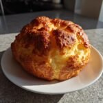 A golden-brown, fluffy cottage cheese cloud bread loaf on a white plate, ready to be served.