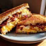 Close-up of an Irresistible Bacon Egg And Cheese Sandwich Delight, cut in half, showing melted cheese, scrambled eggs, and crispy bacon.
