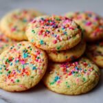A close-up of a stack of Irresistible Birthday Cake Cookies, generously covered in colorful sprinkles.