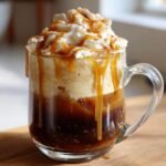 A close-up of an Irresistible Caramel Apple Cider Float topped with whipped cream, caramel drizzle, and cinnamon.