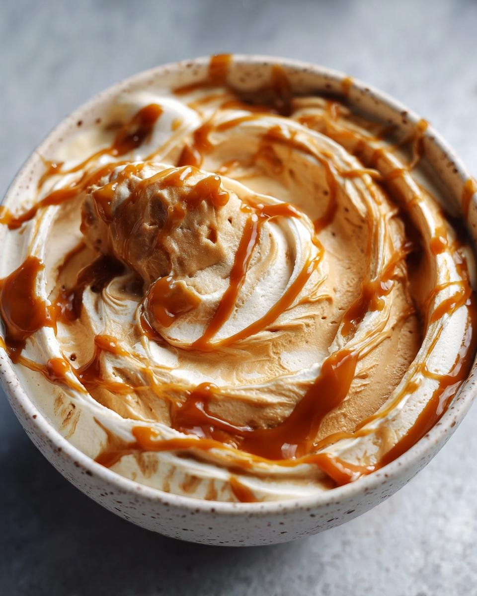 Close-up of Irresistible Caramel Pumpkin Pie Cheesecake Dip swirled with caramel sauce in a speckled bowl.
