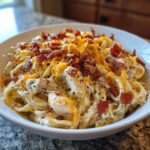 A close-up of irresistible chicken bacon ranch pasta in a white bowl, topped with melted cheddar cheese and crispy bacon bits.