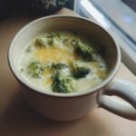 Close-up of a bowl of Irresistible Copycat Panera Broccoli Cheddar Soup, topped with melted cheddar cheese and broccoli florets.