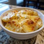 Close-up of a white bowl filled with Irresistible Crockpot Cheesy Potatoes, topped with melted golden cheese.