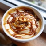 Close-up of a white bowl filled with Irresistible Easy Caramel Pumpkin Pie Cheesecake Dip, drizzled with caramel sauce.