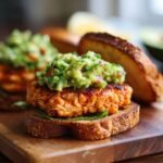 Close-up of an irresistible grilled salmon burger topped with fresh avocado salsa on toasted bread.