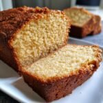 A close-up of a slice of Irresistible Peanut Butter Cake on a white plate, showing its moist crumb and golden crust.