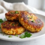 Three golden-brown, pan-fried irresistible salmon cakes with canned salmon recipe, garnished with fresh parsley on a white plate.