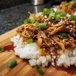 A close-up of Irresistible Slow Cooker Honey Teriyaki Chicken served over white rice, garnished with green onions and sesame seeds.