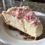A slice of Irresistible White Chocolate Peppermint Cheesecake Mousse Pie topped with crushed candy canes.