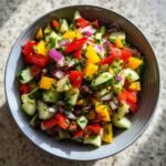 A vibrant bowl of Refreshing Viral TikTok Cucumber Bell Pepper Salad, featuring diced cucumbers, red and yellow bell peppers, red onion, and parsley.