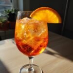 A close-up of a vibrant orange Aperol cocktail filled with ice and garnished with an orange slice.