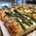 Close-up of a slice of Asparagus Mozzarella Puff Pastry topped with fresh herbs.