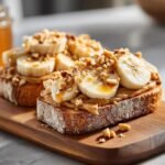 Close-up of Banana Split Breakfast Toast topped with peanut butter, banana slices, chopped nuts, and a drizzle of honey.