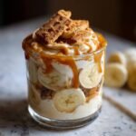 A delicious Biscoff Banana Pudding With Caramel layered in a glass, topped with Biscoff cookies and caramel drizzle.