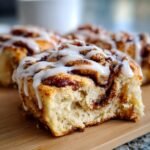 A close-up shot of a soft, gooey Biscoff Cookie Butter Cinnamon Roll with thick white icing drizzled on top.
