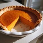 A freshly baked Blender Maple Sweet Potato Pie in a white dish with one slice already cut out.
