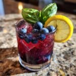 A close-up of a Blueberry Basil Lemon Mocktail with fresh blueberries, basil leaves, and a lemon slice.