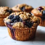 Close-up of a delicious Blueberry Blackberry Jam Muffin with a crumb topping and visible jam oozing down the side.