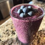 A vibrant Blueberry Coconut Chia Smoothie topped with fresh blueberries in a clear glass.