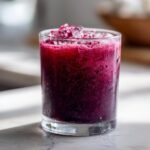 A close-up of a glass filled with vibrant Blueberry Coconut Water Lemonade and crushed ice.