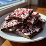 A stack of broken pieces of dark Chocolate Peppermint Bark topped generously with crushed red and white candy canes.