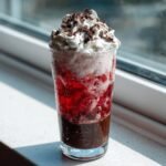 A tall glass containing a layered Chocolate Peppermint Mocktail, topped with whipped cream and chocolate shavings.