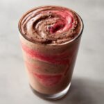 Close-up of a delicious Chocolate Strawberry Protein Smoothie with visible swirls of strawberry puree and chia seeds.