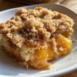 A close-up of a warm serving of Cinnamon Sugar Peach Cobbler Dump Cake with gooey peaches and a crumbly topping.