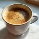 A close-up of a steaming mug filled with a frothy Coconut Chai Latte, with warm sunlight hitting the surface.