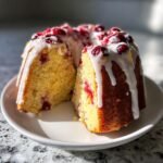 A slice cut from a moist Cranberry Orange Bundt Cake topped with white glaze and whole cranberries.