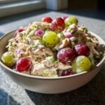 A bowl of Delicious Chicken Salad Chick Grape Salad, featuring shredded chicken, creamy dressing, red onion, and red and green grapes.
