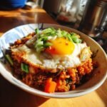 A close-up of a Delicious Egg Roll In A Bowl topped with a sunny-side-up egg and green onions.
