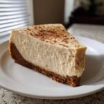 A creamy slice of Eggnog Latte Cheesecake with a thick graham cracker crust, dusted with cinnamon.