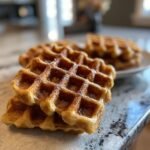 A close-up stack of golden-brown Flourless Vegan Sweet Potato Waffles, lightly dusted with powdered sugar.