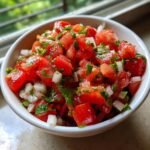 A close-up of a white bowl filled with vibrant Fresh Homemade Pico De Gallo, showing diced tomatoes, onions, and cilantro.