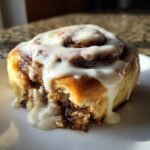 Close-up of a soft Gingerbread Cinnamon Roll generously topped with dripping Eggnog Cream Cheese Glaze.
