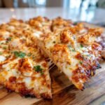 A slice of Hawaiian BBQ Buffalo Chicken Pizza with melted cheese and chicken pieces, garnished with parsley.