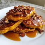 Stack of golden Healthy Pumpkin Quinoa Pancakes topped with rich praline syrup and chopped pecans.